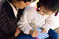 photo of a woman helping a small girl write